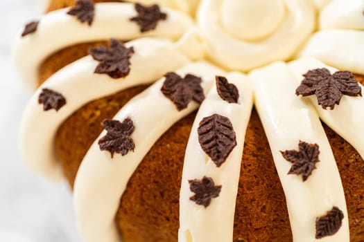 Icing the pumpkin bundt cake with cream cheese frosting and decorating it with chocolate leaves.