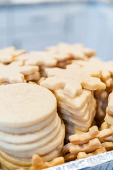Carefully stacking the beautifully crafted snowflake-shaped sugar cookies into a foil pan, ready for freezing as delightful Christmas treats.