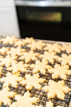Letting delightful snowflake-shaped sugar cookies cool on a rack, preparing them for festive Christmas gifts.