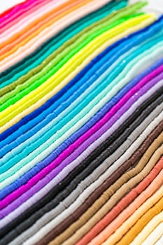 A vibrant collection of clay beads, neatly arranged by color on a white table, ready to inspire young crafters to create their own unique bracelets.