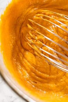 A close-up view of expertly blended ingredients in a large mixing bowl for a mouthwatering homemade pumpkin bundt cake.
