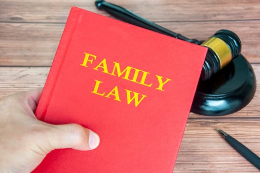 Hand holding Family Law book with gavel on wooden table background.
