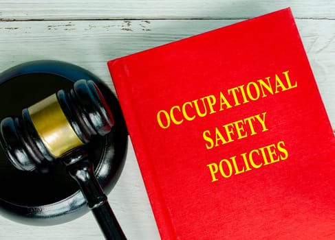 Top view of Occupational Safety policies text on red cover book with gavel background.