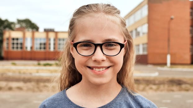 Happy student wearing eyeglasses, smiling brightly while standing in front of a school building, radiating joy and positivity