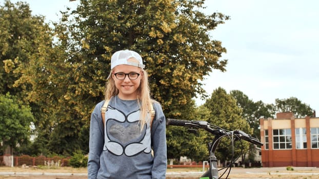 An 11 year old girl shows her thumbs up in a good mood next to her bicycle in the summer