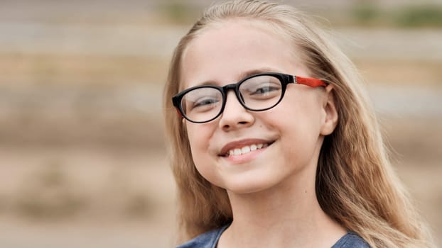 Close up portrait of a cheerful school girl wearing eyeglasses, enjoying her time outdoors and smiling happily