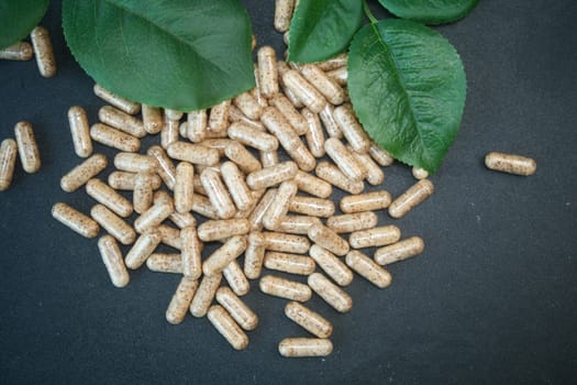 Natural dietary capsules rest on a smooth dark surface next to vibrant leaves.