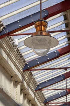 Windsor, England - Apr 3, 2025 - A vintage copper ceiling light fixture with a glass globe shade hangs from a white ceiling and Wooden beams are visible creating a rustic yet elegant interior atmosphere at Windsor & Eton Riverside railway station. Paddington pendant light, use it as your Wallpaper, Poster and Copy space, Selective focus.