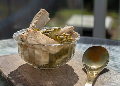 Boiled bitter gourd soup (Boiled bitter melon soup) with Pork spare rib in Glass bowl served with Brass spoon on Wooden cutting board. use it as your Wallpaper, Poster, Design and Space for text, Selected focus.