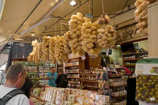 Crete, Greece - April 5, 2025: Local stall displaying clusters of natural sponges wrapped in plastic, surrounded by jars of honey and packaged goods in a lively market ambiance.