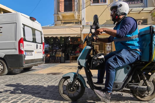 Crete, Greece - April 5, 2025: Urban delivery scene with a Wolt partner navigating the streets on a scooter with a visible branded bag, surrounded by Mediterranean architecture and bright skies.