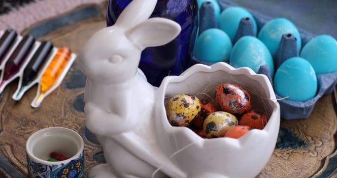 A festive setup showcases an Easter Bunny shaped bowl filled with vibrant Easter eggs and quail eggs. Nearby are coloring tools ready for decorating eggs.