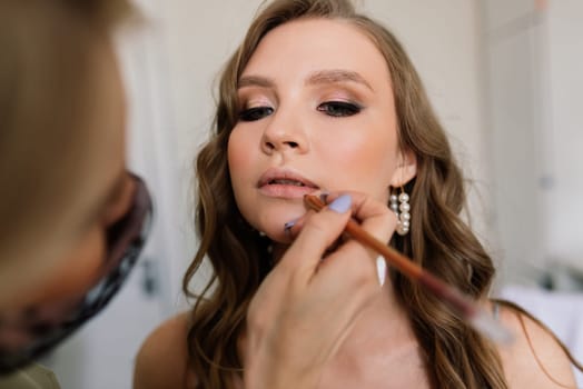 Makeup artist applies lipstick. Hand of make-up master, painting lips of a young beauty model.