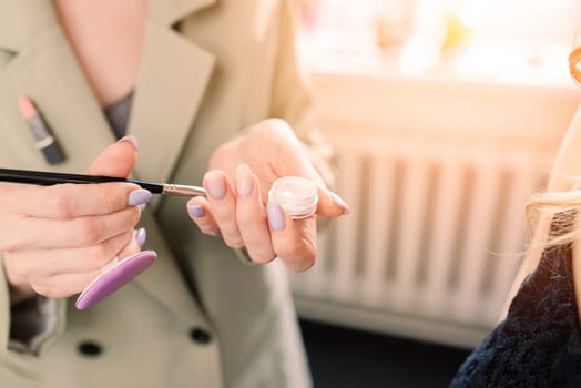 Makeup artist applies lipstick. Hand of make-up master, painting lips of a young beauty model.