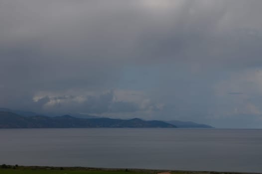 A tranquil coastal view unfolds beneath dramatic clouds, where gentle waves meet the shoreline. The muted colors evoke a peaceful atmosphere, inviting mindful contemplation and appreciation.