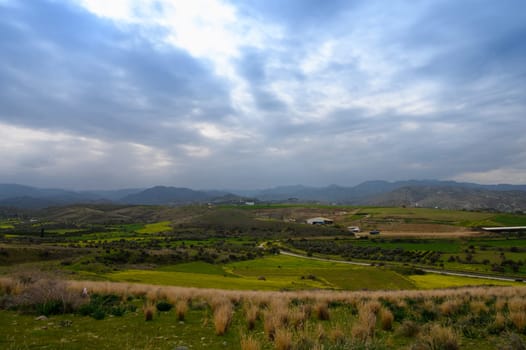 Beneath a blanket of swirling clouds, lush green hills stretch across the horizon, inviting exploration in a tranquil countryside setting. Nature thrives in this serene vista.