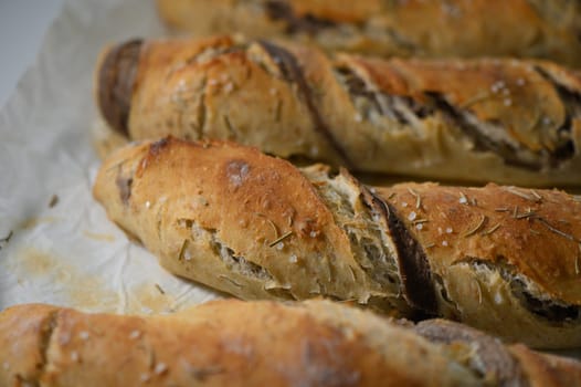 These delightful, freshly baked artisan bread loaves are adorned with a golden crust and sprinkled with aromatic herbs, exuding irresistible warmth and fragrance in a cozy kitchen setting.