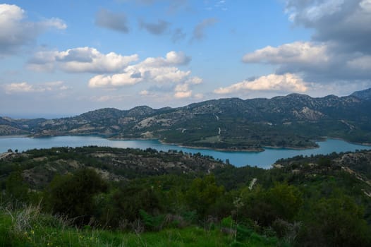 A serene lake reflects the soft hues of the afternoon sky, framed by rolling mountains and lush greenery. Nature's beauty captivates the senses in this peaceful moment.