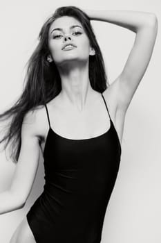 Stylish woman in a black swimsuit strikes a dynamic pose against a neutral backdrop, embodying confidence and elegance. Perfect for fashion and beauty themes.
