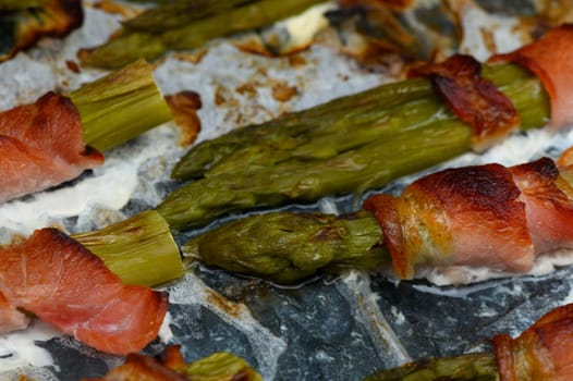 Succulent asparagus spears are artfully wrapped in crispy bacon, sizzling on a grill during an inviting sunset gathering. The aroma fills the air, creating a warm atmosphere for sharing.
