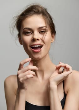 Cheerful young woman exuding confidence with a bright smile and playful gesture. The light gray background complements her casual style and lively emotion.