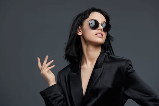 Woman, black suit, sunglasses a confident woman in a sleek black suit and stylish sunglasses poses for the camera with one hand on her hip while placing a finger on her lips, exuding sophistication