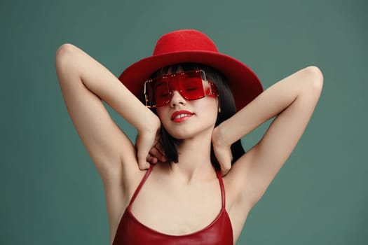 Red hat, sunglasses, woman, posing a confident woman in a red hat and stylish sunglasses poses for the camera with her hands on her head and her arms behind her back, exuding chic and playful energy