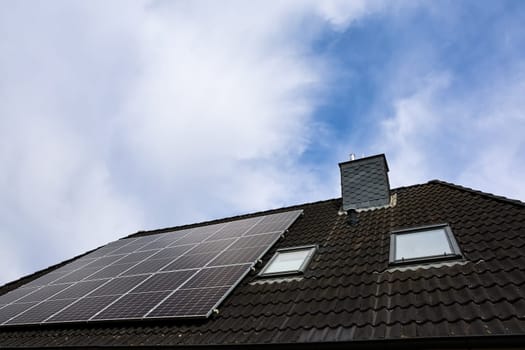 Photovoltaic panels installed on a rooftop with chimney and skylights, providing clean energy under a cloudy sky