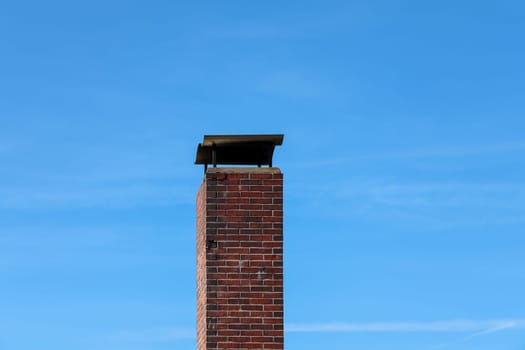 Red brick chimney rising tall with a sleek metallic chimney cowl, set against a backdrop of a vibrant clear blue sky