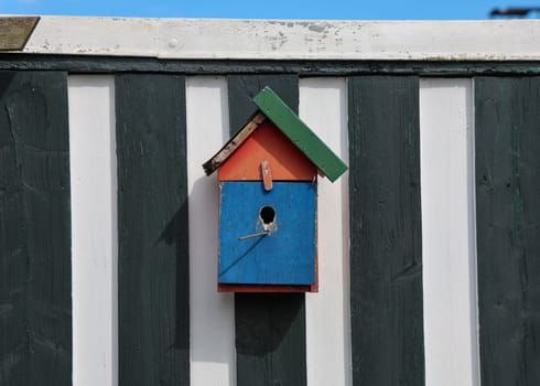 Brightly colored birdhouse adds a touch of whimsy to a striped wooden fence, providing a welcoming home for feathered friends