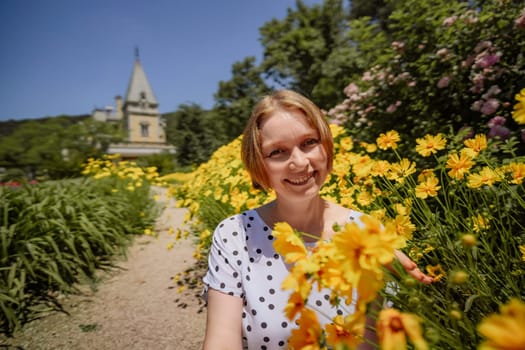 A woman is sitting in a field of yellow flowers. She is smiling and looking at the camera
