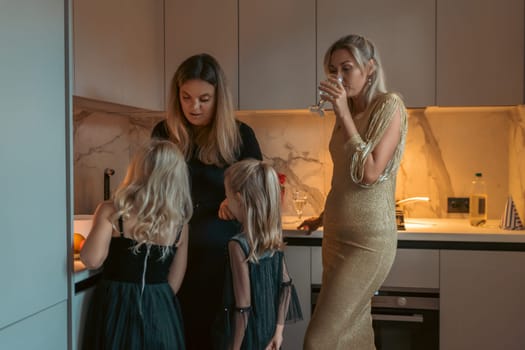 Three women and two young girls in a modern kitchen. One woman drinks from a glass others attend to children. Warm lighting.