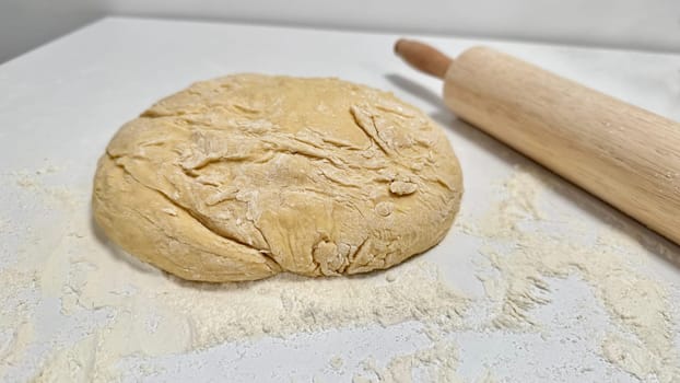 Fresh Dough Ready for Baking with a Rolling Pin and Flour Dusting. Raw dough ball on a floured surface, accompanied by a wooden rolling pin, set for baking preparations. Captures the essence of baking creativity and culinary inspiration.