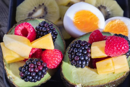 Vibrant healthy food with blackberry, redberry and mango on avocado with golden kiwi and boiled egg is eating colorful on ceramic dish. Breakfast plate with fruits, use it as your space for text, design, wallpaper and poster.