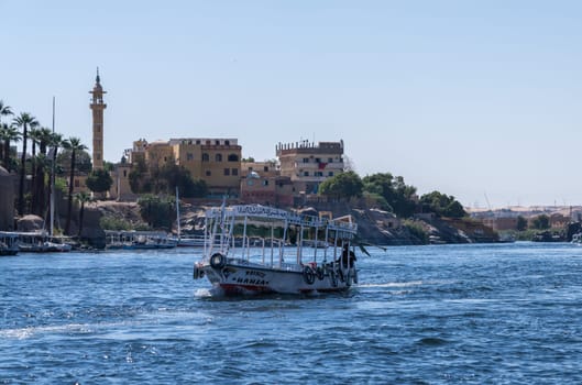 Aswan, Egypt - 4 November 2024: Ferry boat approaches the dock on the Nile with mosque and homes on the shore