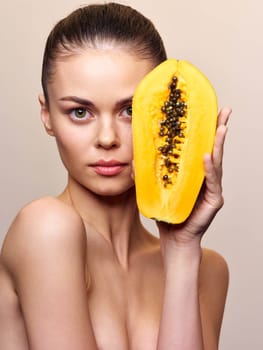 Woman holding a ripe papaya in front of her face and looking at the camera in a tropical setting