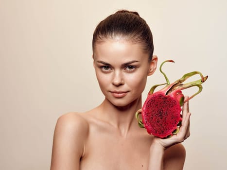 Attractive woman holding a fresh dragon fruit slice on beige background in natural lighting