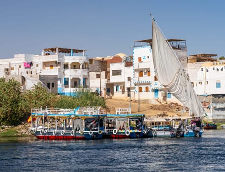 Homes line the shores of Nile on Elephantine island with ferry boats and cruise boats docked alongside in Aswan
