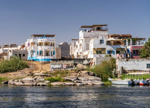 Homes line the shores of Nile on Elephantine island with ferry boats and cruise boats docked alongside in Aswan