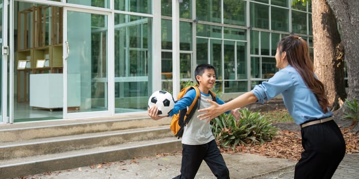 An excited boy runs toward his mother who's waiting with open arms, celebrating his return from school, holding a soccer ball.