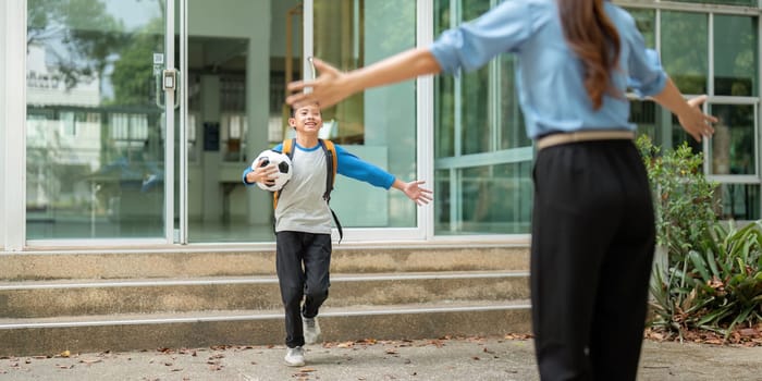 A happy child runs to embrace a parent after school, holding a soccer ball, highlighting the warmth of family reunions and the excitement of home.