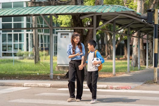 A young boy holds a soccer ball and crosses the street with his teacher, illustrating the connection and support they share as school begins.