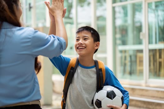 A joyful boy high-fives his teacher outside a school, excited about returning to classes and playing soccer. This captures the spirit of enthusiasm for learning and sports.