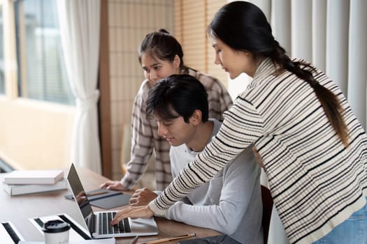 In a vibrant learning environment, students huddle around a laptop, engaging in research and discussions to enhance their understanding of the subject matter.