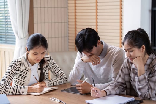 Three students work together at a table, deeply focused on their studies. The scene captures their dedication and collaboration as they take notes and discuss questions.