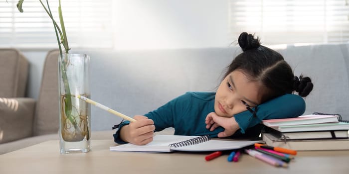 In a moment of distraction, a young girl rests her head on her hand, looking contemplative as she tries to write, illustrating the challenges of maintaining focus.