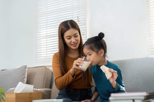 A loving mother shares a moment with her daughter, offering her a glass of milk and a sandwich as they prepare for a productive day.