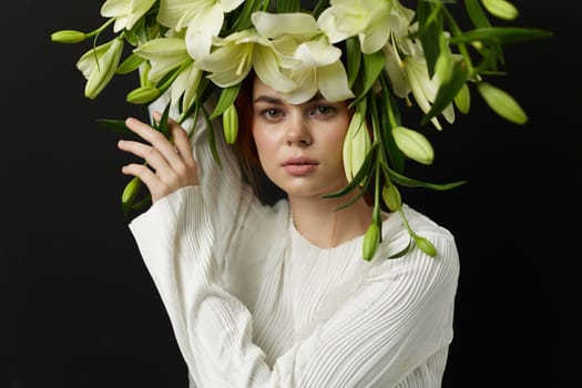 A young woman styled in a white outfit showcases a crown of flowers, embodying tranquility and elegance against a dark background, emphasizing nature s beauty