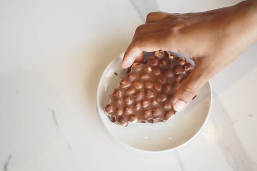 A hand lifts a chocolate treat from a small white plate.