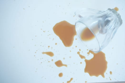 A cup tipped over, spilling a brown liquid across a white surface.